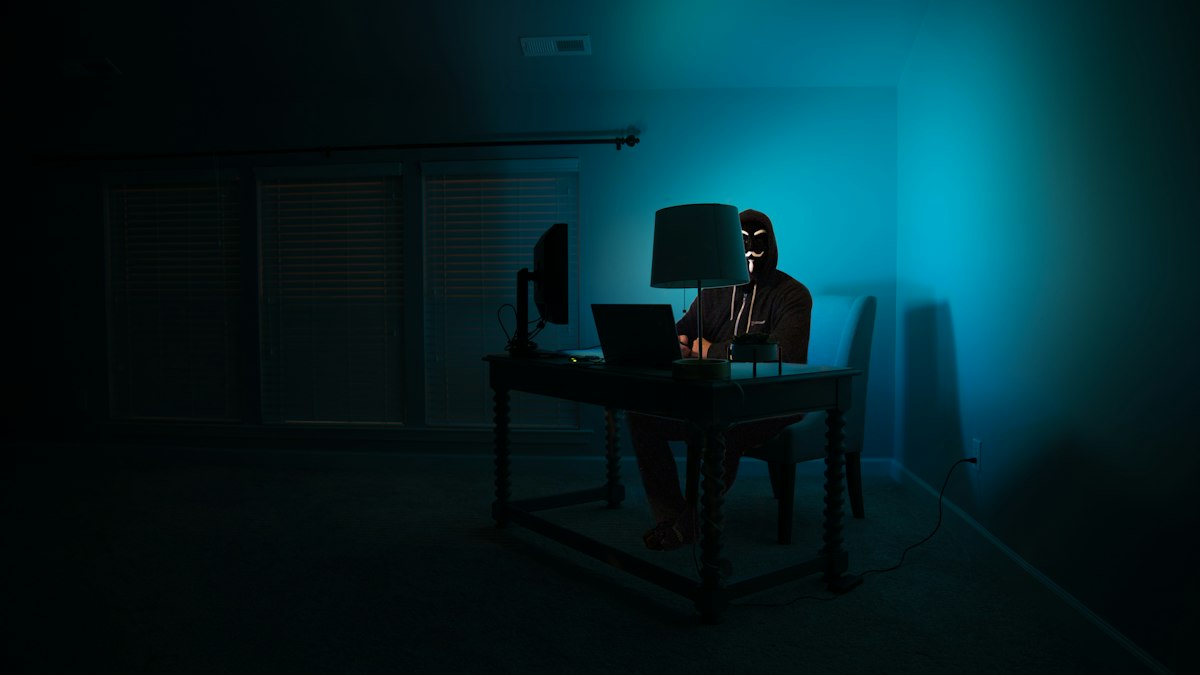 Karanlık odada bilgisayar başında maskeli kişi (Hooded person at a computer in a dark room)