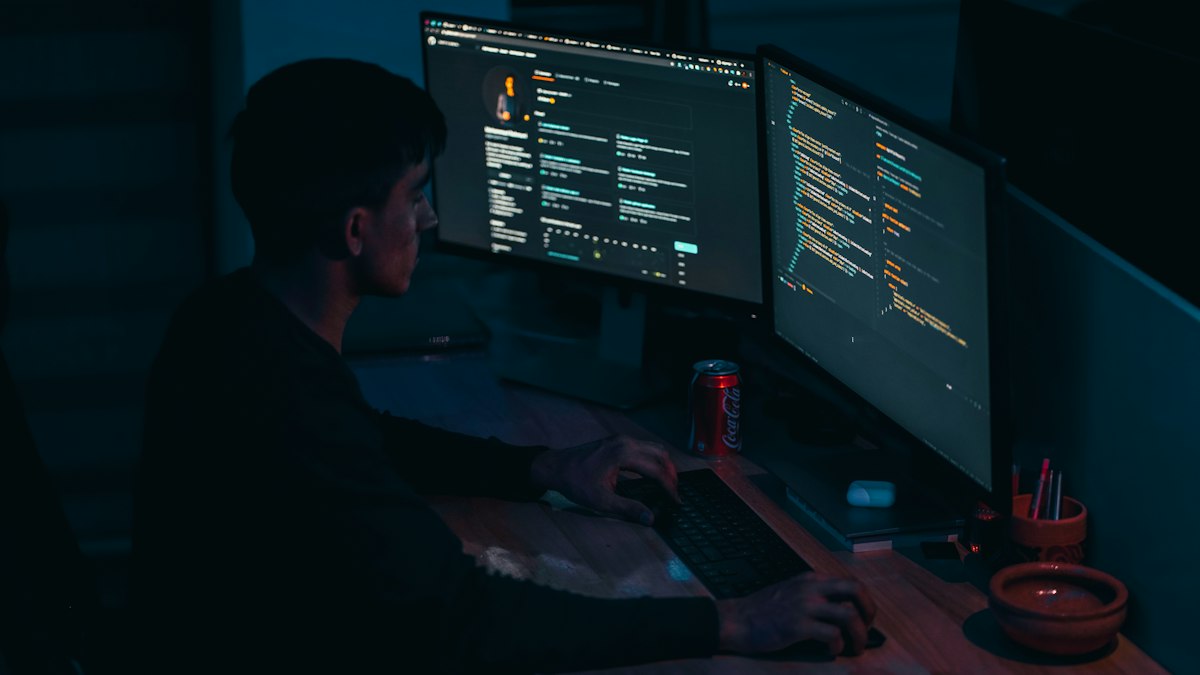 Gece çift monitörde kod yazan geliştirici (Developer coding on two monitors at night)