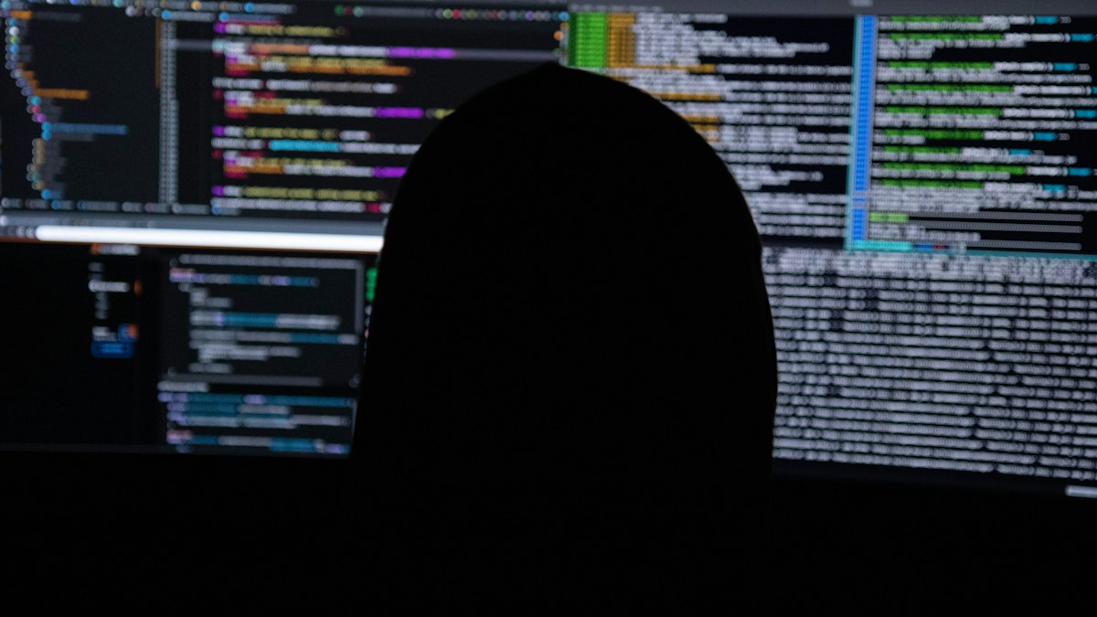 Kod görüntülenen ekranların önünde siluet (Silhouette in front of monitors displaying code)